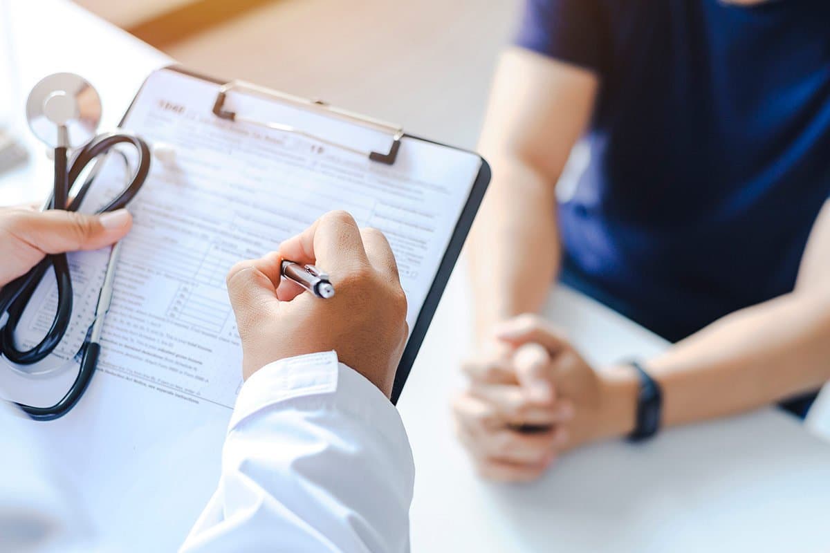 Un médecin remplissant un formulaire sur un clip-board lors d'une consultation avec un patient.